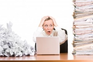 Frustrated woman at computer with paper stacked around her